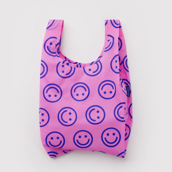 A small nylon shopping back in hot pink with blue smiley faces on a white backdrop.