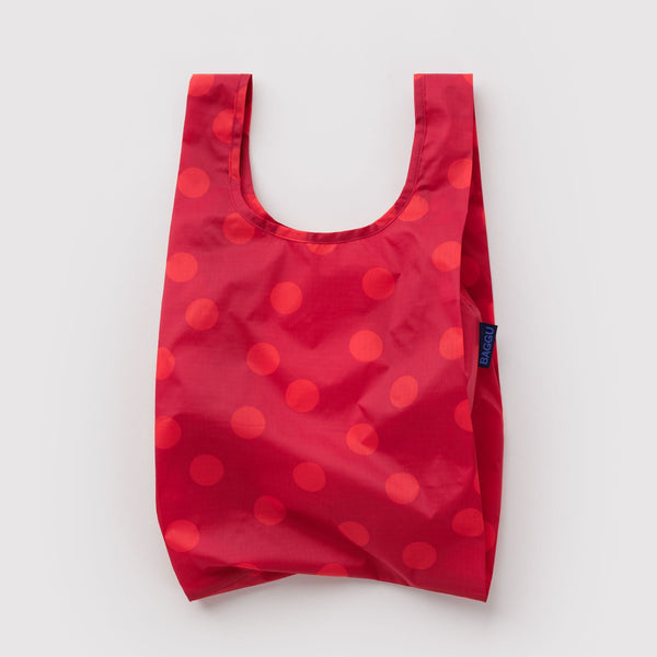 A small nylon shopping bag in red with lighter red polka dots against a white backdrop.