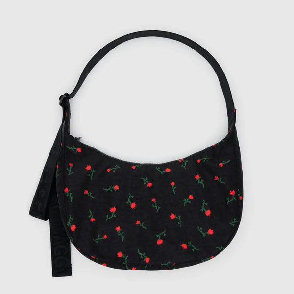 A black nylon half moon crossbody bag with a dainty red and green wildflower print on a white background.