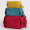A stack of three expandable nylon packing cubes in bold solid tones of yellow, teal, and red against a white background.