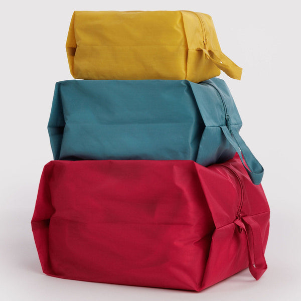 A stack of three expandable nylon packing cubes in bold solid tones of yellow, teal, and red against a white background.