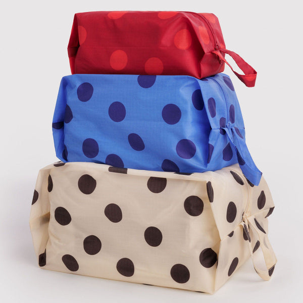 A stack of three expandable packing cubes in various colors of large polka dots against a white background.