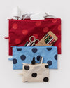 Three fabric zip pouches with polka dots are arranged on a light gray background. The top pouch is red with red polka dots and contains white charging accessories. The others include various pens, pencils, scissors, and other small items. 