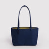 A navy blue nylon tote bag with shoulder straps, a charm leash, and a bright yellow interior that is the other side of this reversible design.