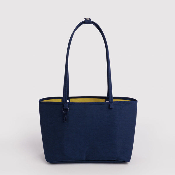 A navy blue nylon tote bag with shoulder straps, a charm leash, and a bright yellow interior that is the other side of this reversible design.
