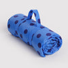 Rolled-up blue nylon picnic blanket with dark polka dots on a light gray background