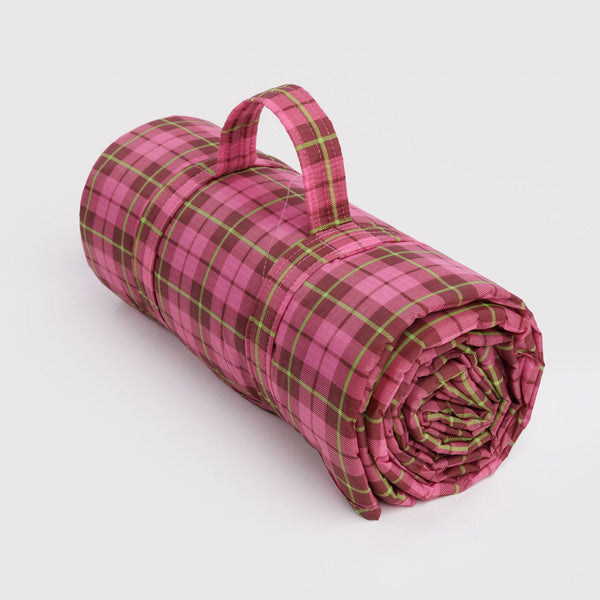 A rolled-up pink and green plaid ripstop picnic blanket with a carrying handle on a white background.