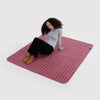 A person sitting on a pink and green plaid ripstop picnic blanket against a white background.