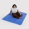 A person sitting on a blue and navy polka dot nylon picnic blanket against a white background.