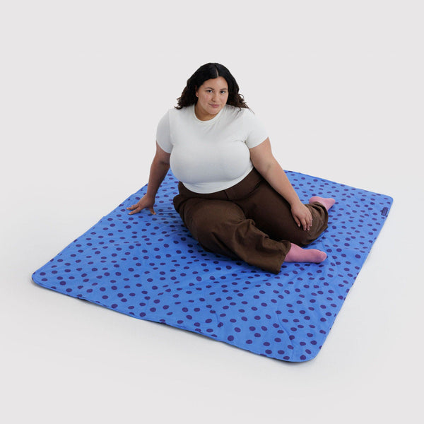 A person sitting on a blue and navy polka dot nylon picnic blanket against a white background.