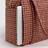 A close-up view of a brown houndstooth carry-on bag with a laptop slid into a back pocket against a white background.