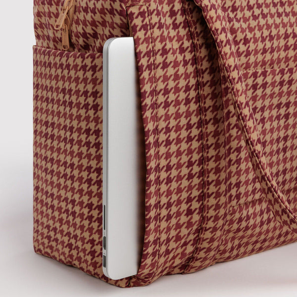 A close-up view of a brown houndstooth carry-on bag with a laptop slid into a back pocket against a white background.