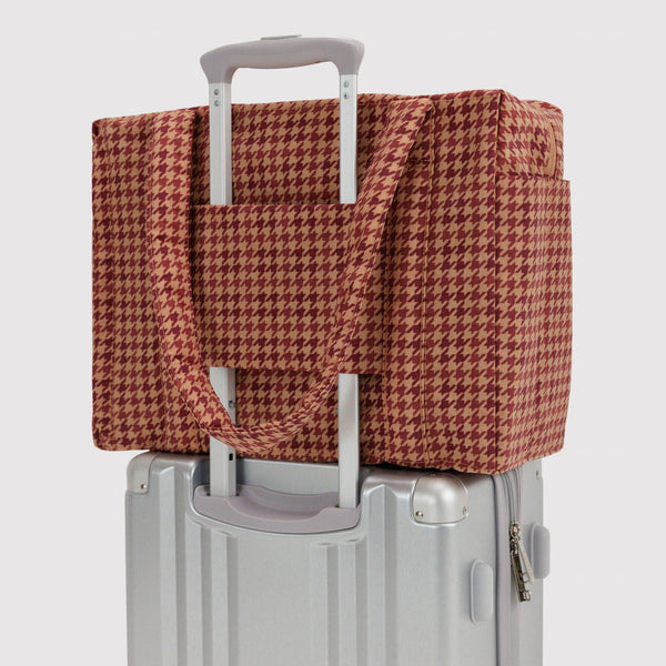 A brown houndstooth carry-on bag attached to the extended handle of a rolling suitcase against a white background.