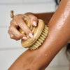 Person using a dry brush on their arm with a neutral background