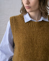 A close-up view of a person wearing a bronze handknit crewneck pullover sweater vest styled over a light blue and white striped shirt.