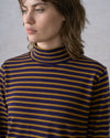 A close-up view of a person wearing a long sleeve mockneck knit top in dark navy and bronze stripes against a white background.