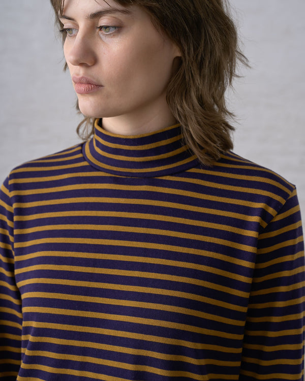 A close-up view of a person wearing a long sleeve mockneck knit top in dark navy and bronze stripes against a white background.