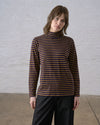 A person standing against a white wall wearing a long sleeve dark navy and bronze striped knit top with a mockneck collar, styled over black pants.