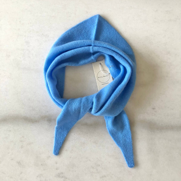 A bright baby blue fuzzy cashmere-wool blend triangle cravat scarf looped against a white marble backdrop.