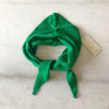 A bright emerald green cashmere-wool blend triangle cravat scarf looped against a white marble backdrop.