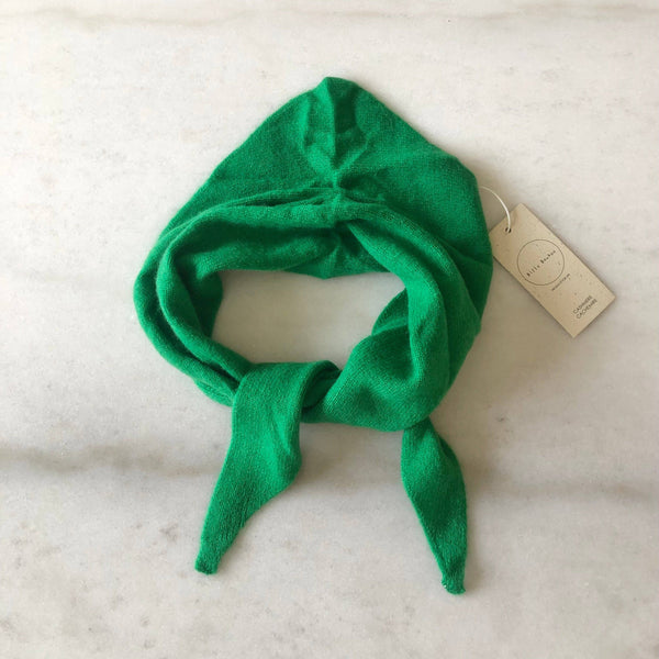 A bright emerald green cashmere-wool blend triangle cravat scarf looped against a white marble backdrop.