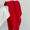 A close up view of a fuzzy cashmere-wool blend bright red cravat scarf being held up against a white wall.