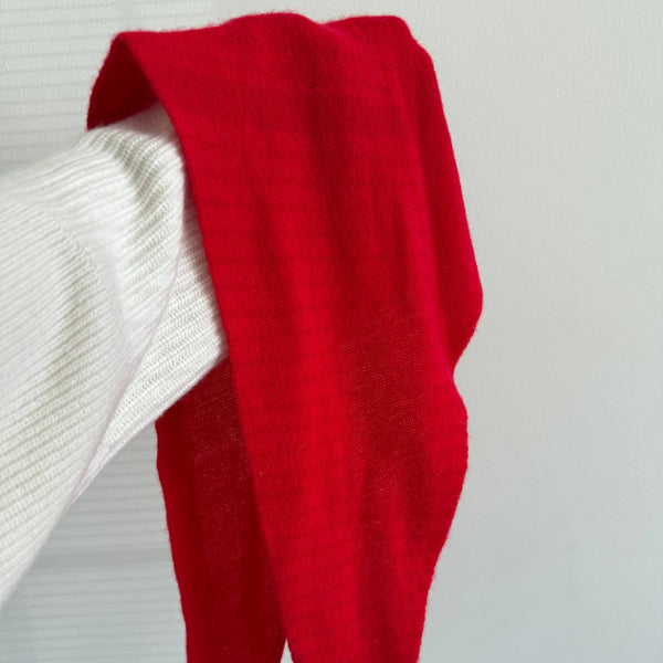 A close up view of a fuzzy cashmere-wool blend bright red cravat scarf being held up against a white wall.