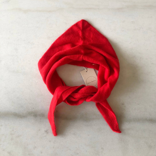 A bright red fuzzy cashmere-wool blend triangle cravat scarf looped against a white marble backdrop.
