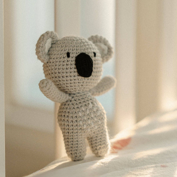 Crocheted koala rattle toy on a soft surface with a blurred background