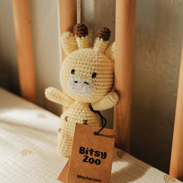 Crocheted giraffe rattle toy with a 'Bitsy Zoo' tag on a wooden surface
