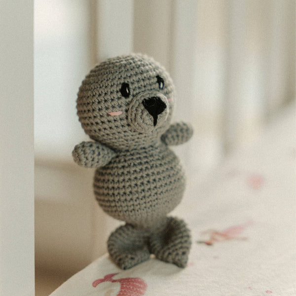 Crocheted seal rattle toy on a soft surface with a blurred background