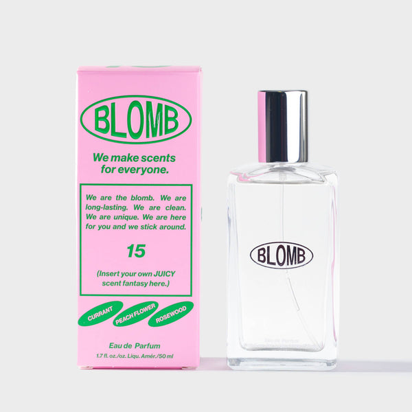 A clear rectangular perfume bottle with a reflective silver cap stands next to its pink packaging box. Both the bottle and box feature the brand name 'BLOMB' in green and black lettering, indicating scent number 15.