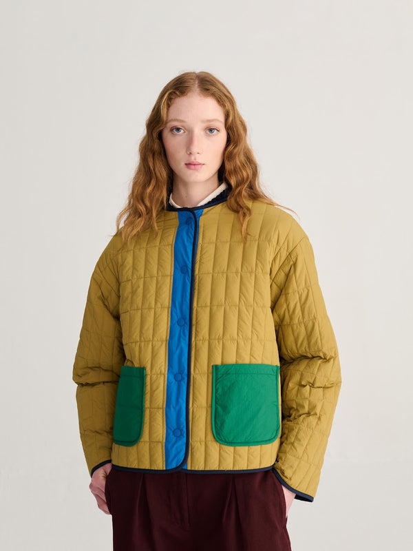 A person wearing a tan, blue and green colorblock lightweight puffer jacket and brown pants against a white background.