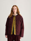 A person wearing a dark red and mustard yellow colorblock jacket, the reverse side.
