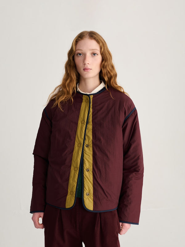A person wearing a dark red and mustard yellow colorblock jacket, the reverse side.