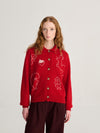 A model wearing a red sweater with a white forest scene and dark red pants against a white wall.