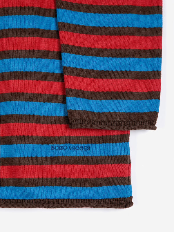 A close-up detail of the sleeve cuff nd embroidered 'Bobo Choses' hem detail on a bright red blue and brown striped button up cardigan against a white background.