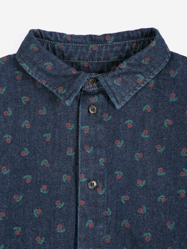 A close-up detail of a dark wash denim collared shirt with a subtle red and green floral print against a white background.