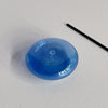 A translucent blue bubble-shaped glass incense holder with a stick of incense laying next to it against a neutral background.
