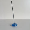 A translucent blue bubble-shaped glass incense holder holding a stick of incense against a neutral background.