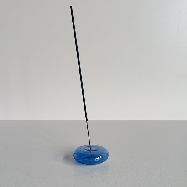 A translucent blue bubble-shaped glass incense holder holding a stick of incense against a neutral background.