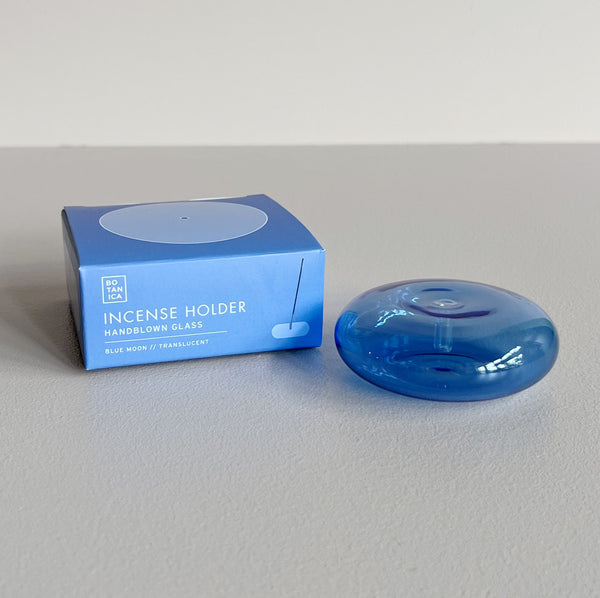 A translucent blue bubble-shaped glass incense holder next to its packaging on a neutral background.