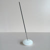 A white milk glass bubble-shaped incense holder holding a stick of incense against a neutral background.