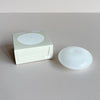 A white milk glass bubble-shaped incense holder next to its packaging against a neutral background.