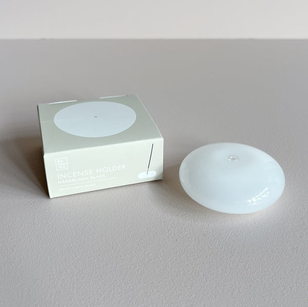 A white milk glass bubble-shaped incense holder next to its packaging against a neutral background.