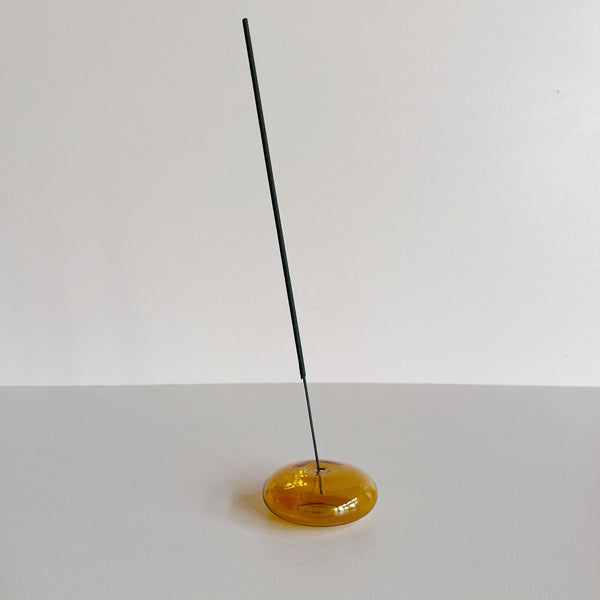 A translucent amber glass bubble-shaped incense holder with a stick of incense against a neutral background.