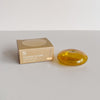A translucent amber glass bubble shaped incense holder sitting next to its packaging on a neutral backdrop.