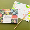 Forest Floor 10 Minute Creative Escape art book shown with a partially colored page, and a paintbrush on an olive green background.