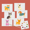 Set of postcards with watercolor illustrations of dogs along with a paintbrush and dry dot watercolor palette against a rust red background.
