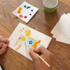 Kid painting a dog postcard with watercolors on a wood table.